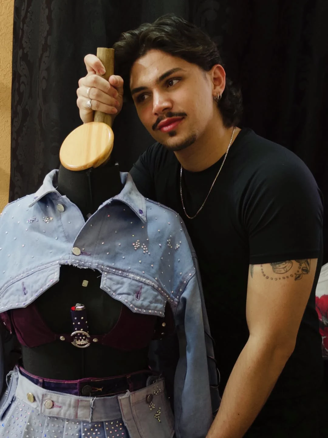 Criador ao lado do manequim com look de jeans claro e roxo.